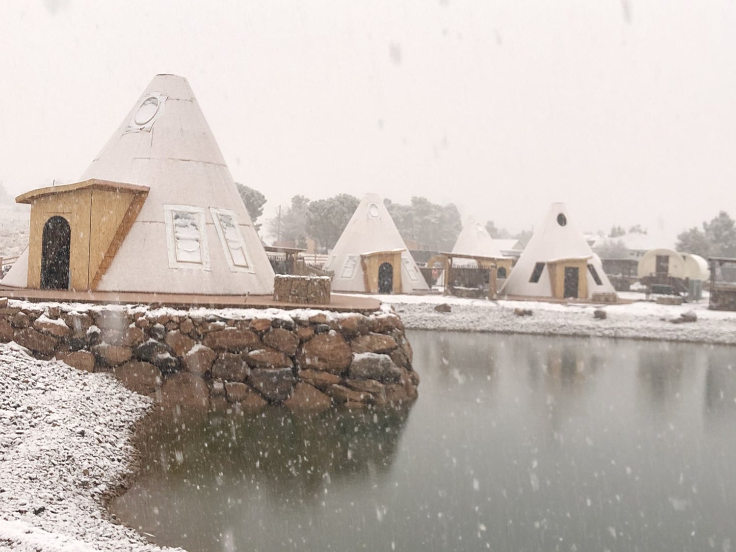 Snow-covered teepee structures beside a pond
